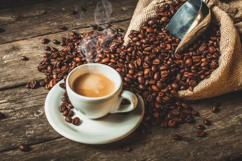 A cup of coffee next to a large pile of coffee beans