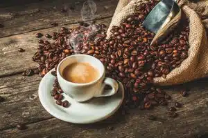 A cup of coffee next to a large pile of coffee beans